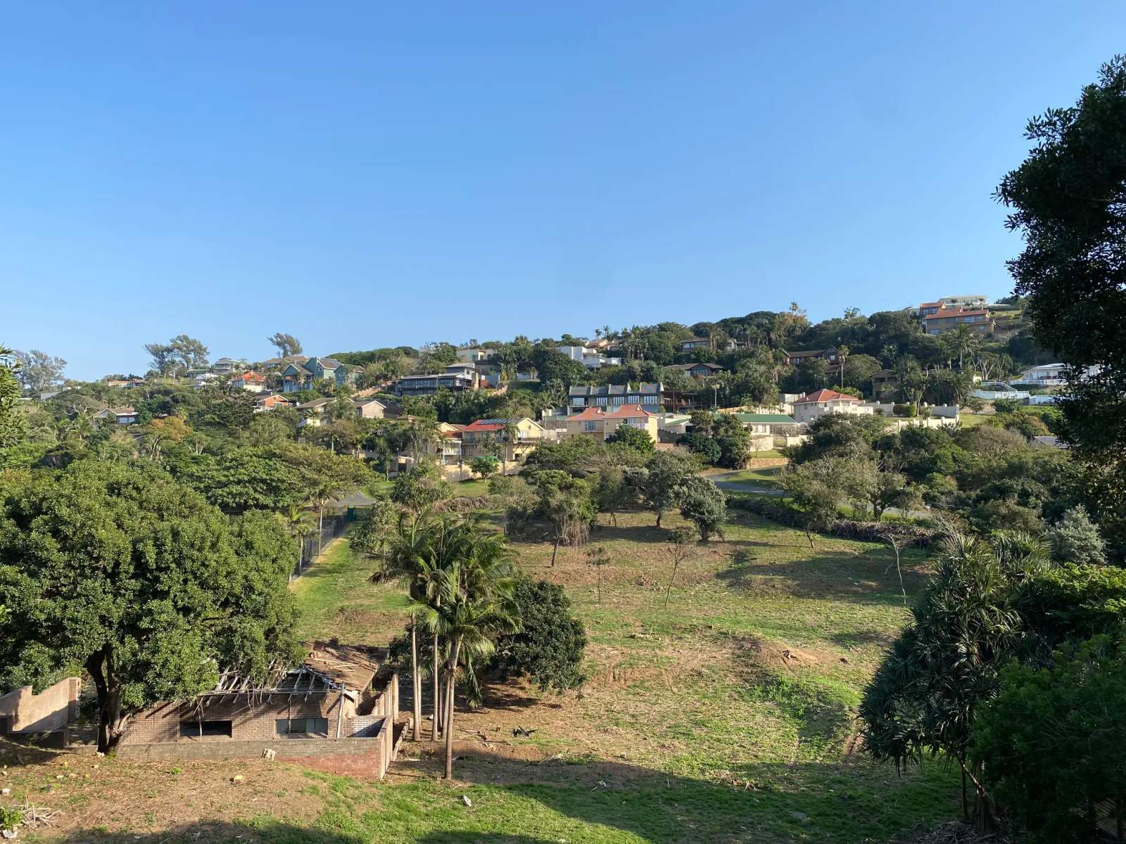 Houses nestled on a lush, green hillside against a blue sky in Zinkwazi.