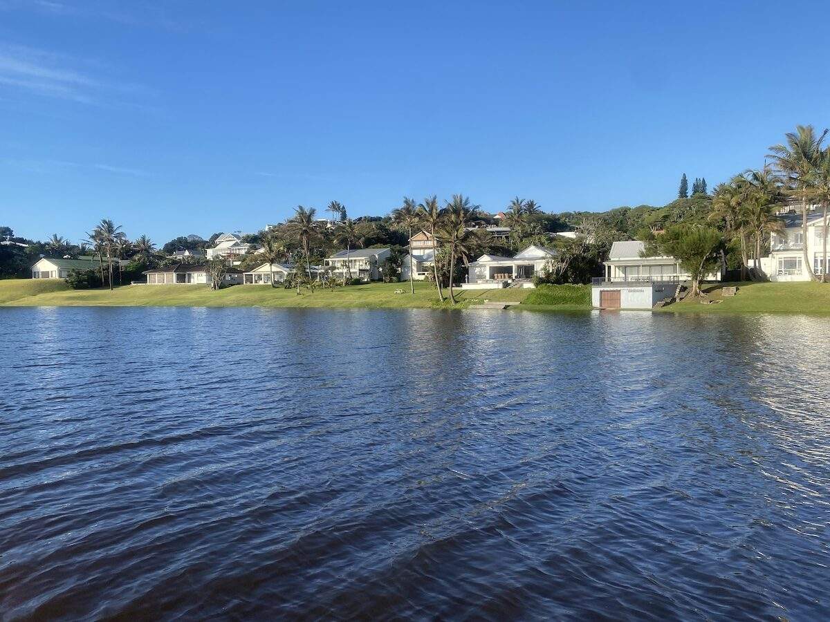 Lagoon with waterfront houses and palm trees lining the shore in Zinkwazi under a clear blue sky.